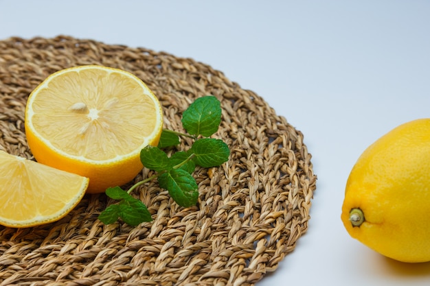 Foto gratuita limones frescos con hojas en blanco y estera de mimbre