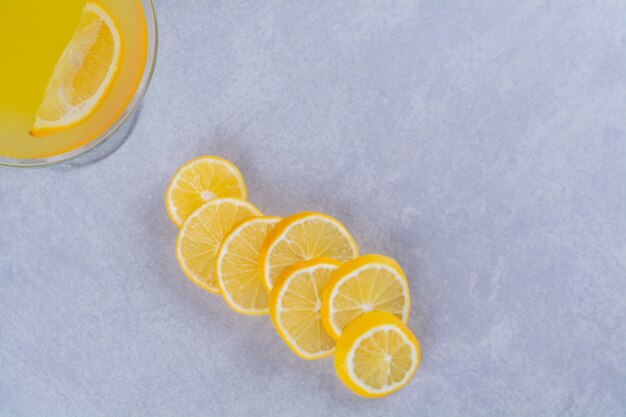 Limones frescos en rodajas junto a un vaso de jugo de naranja en la mesa de mármol.