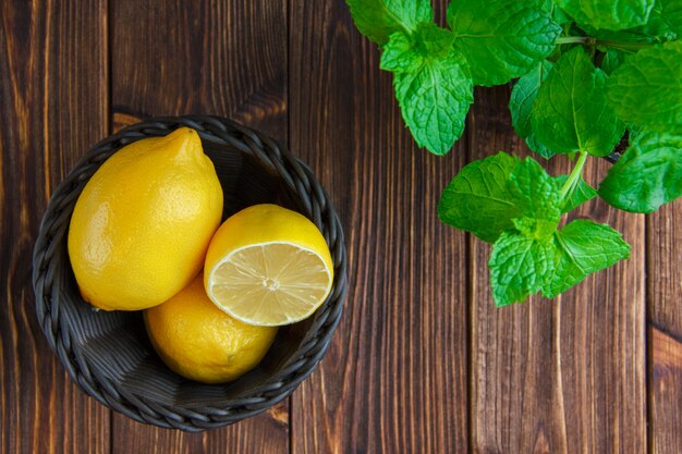 Limones con hierbas en una cesta de mimbre sobre mesa de madera, plana.