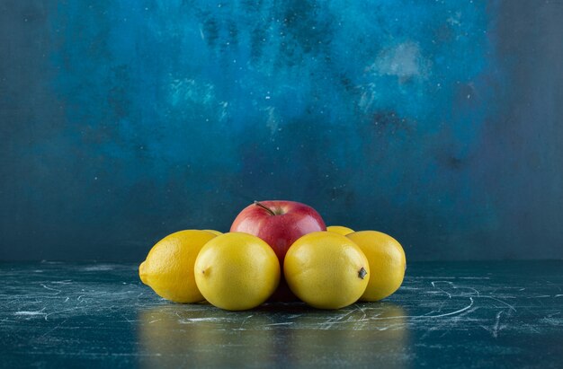 Limones jugosos y manzana roja sobre mesa de mármol.