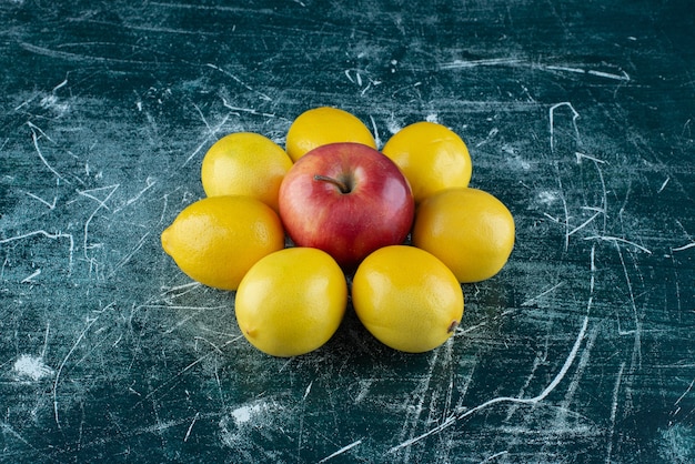 Limones jugosos y manzana roja sobre mesa de mármol.