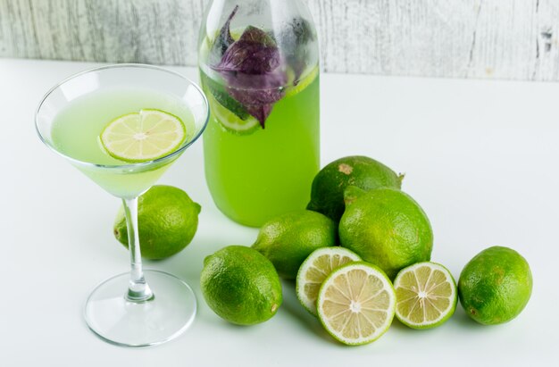 Limones con limonada, hojas de albahaca en blanco y sucio, vista de ángulo alto.