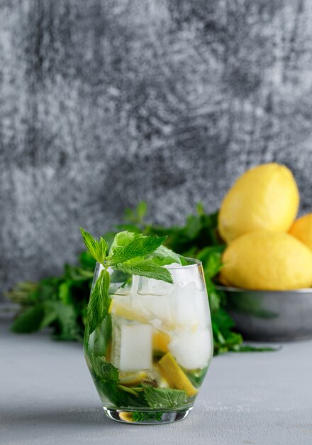 Limones y menta en un recipiente con agua helada de desintoxicación vista lateral sobre grunge y superficie gris