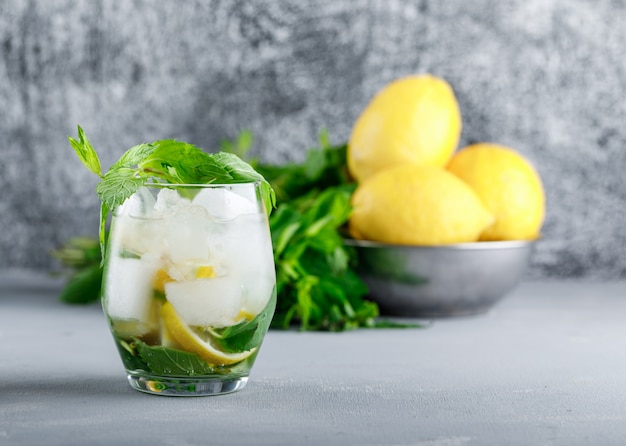 Limones y menta en un recipiente con agua helada de desintoxicación vista lateral sobre grunge y superficie gris