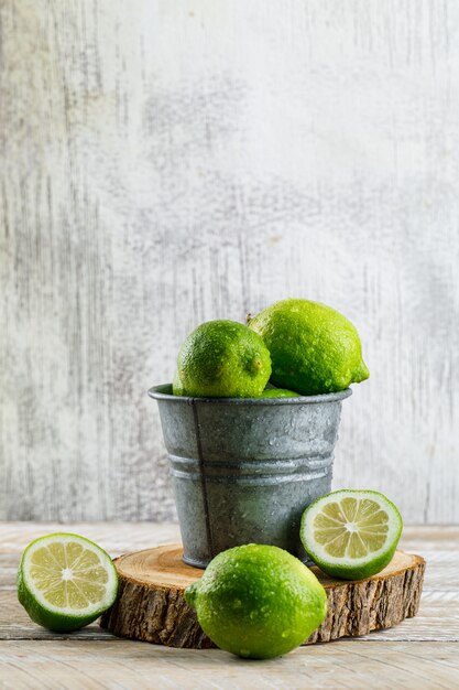 Limones en un mini cubo con vista lateral de tabla de cortar en madera y sucio