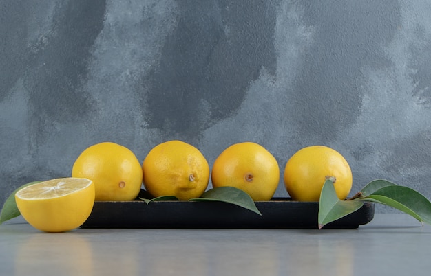 Limones en una pequeña bandeja adornada con hojas sobre mármol