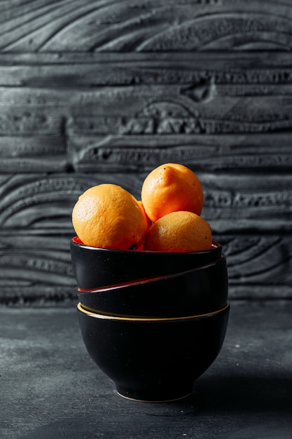 Limones en un recipiente sobre un fondo oscuro de la madera. vista lateral. espacio para texto