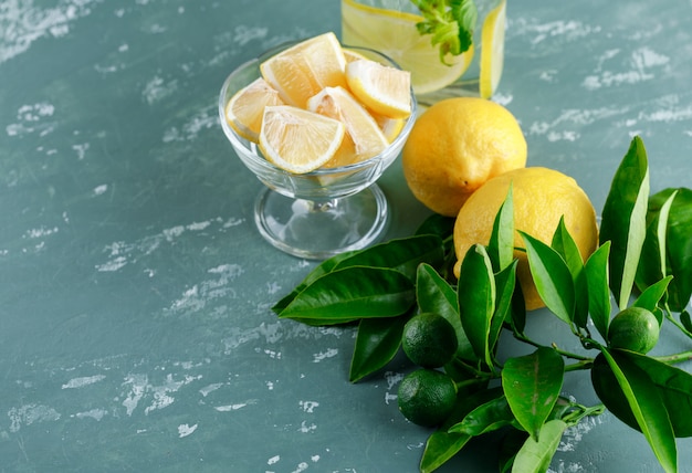 Limones con rodajas, hojas, agua de desintoxicación en la superficie de yeso