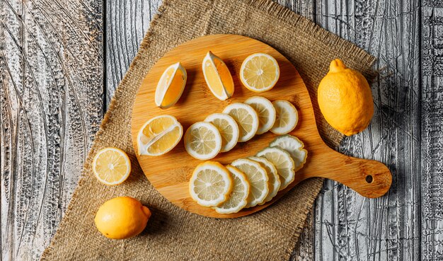 Limones con rodajas vista superior sobre una tabla para cortar, tela y fondo oscuro