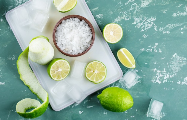 Limones con sal, cubitos de hielo sobre yeso y tabla para cortar,