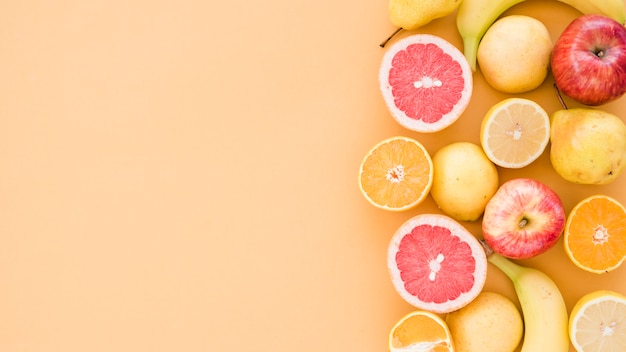 Foto gratuita limones de sección transversal; naranja; manzana; peras y plátano sobre fondo beige