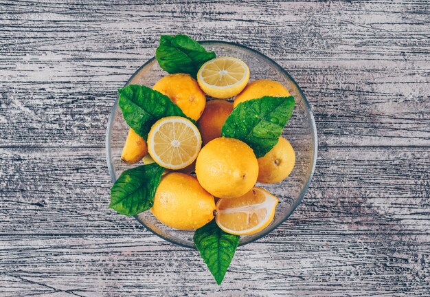 Limones en un tazón con rodajas y hojas vista superior sobre un fondo de madera gris