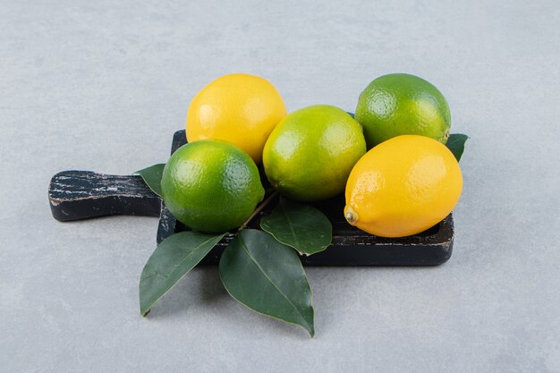 Limones verdes y amarillos sobre tabla de cortar negra.