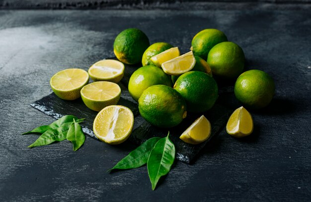 Limones verdes con rodajas vista de ángulo alto sobre un fondo negro con textura