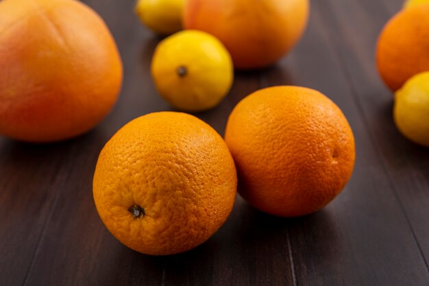 Limones de vista frontal con naranjas y pomelos sobre fondo de madera