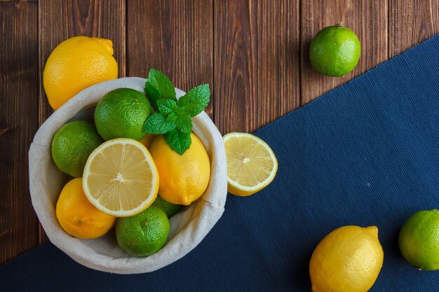 Limones de vista superior en canasta con paño azul sobre superficie de madera. espacio vertical para texto