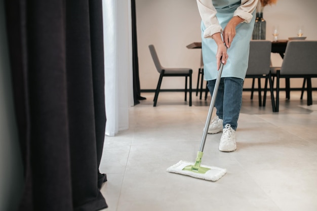 Limpieza de la cocina. Una mujer joven en delantal limpiando el piso en la cocina