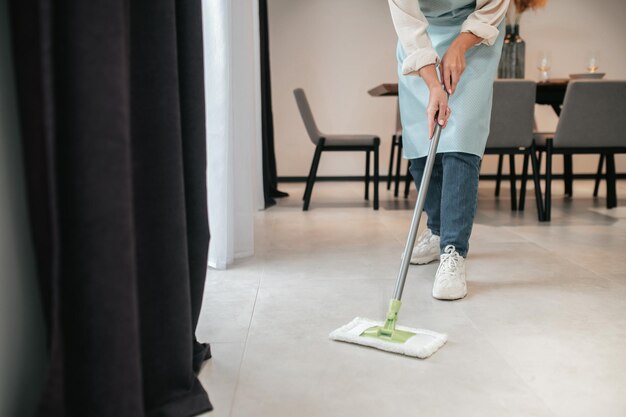 Limpieza de la cocina. Una mujer joven en delantal limpiando el piso en la cocina