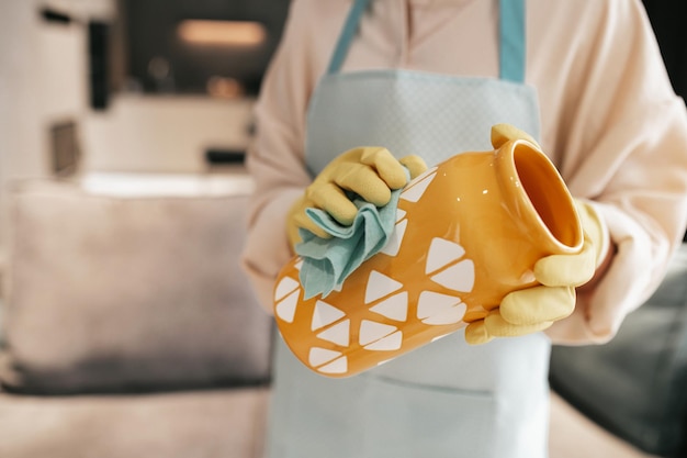 Limpieza de vajilla. Una mujer con guantes limpiando un jarrón naranja.