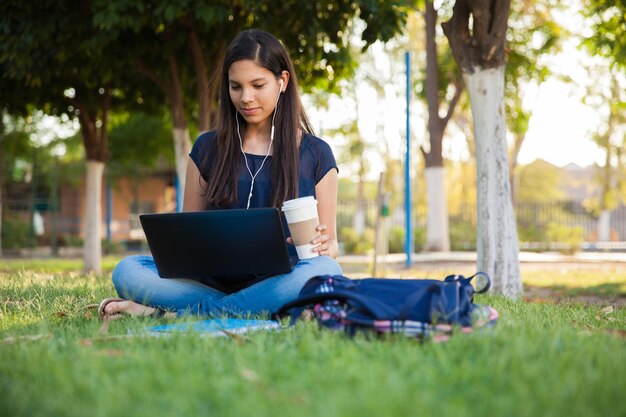 Una linda adolescente hispana usando una laptop y bebiendo café al aire libre