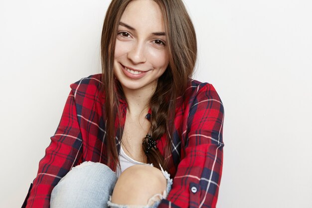 Linda adolescente mirando a la cámara y sonriendo tímidamente abrazando sus rodillas