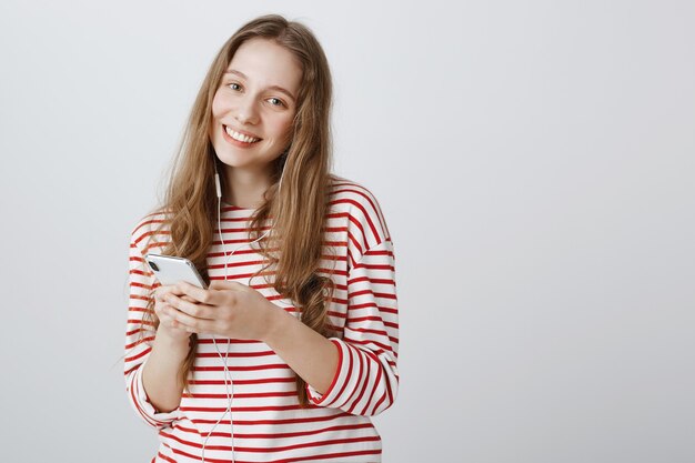 Linda adolescente usando teléfono móvil y escuchando música en auriculares