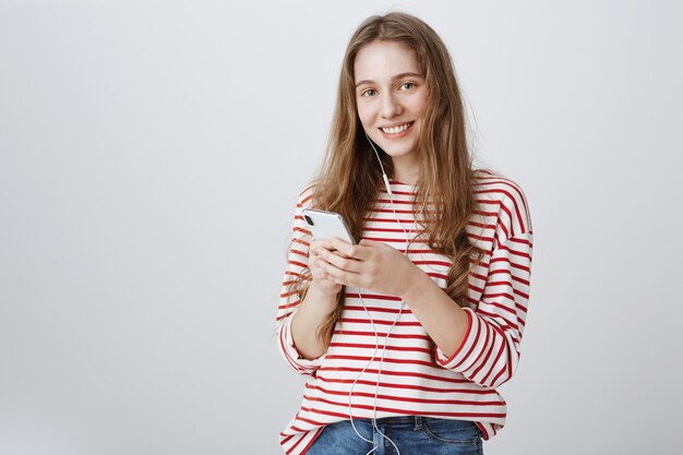 Linda adolescente usando teléfono móvil y escuchando música en auriculares