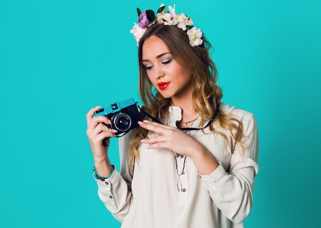 Linda alegre rubia fresca mujer con corona de flores en la cabeza posando en primavera elegante traje tomando foto sobre fondo azul brillante. Usando tierna corona floral, ropa de primavera.