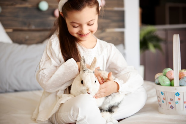 Foto gratuita linda chica acariciando conejo esponjoso en la cama