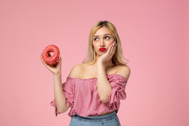 Linda chica adorable chica con lápiz labial rojo en blusa rosa pensando en algo con donut