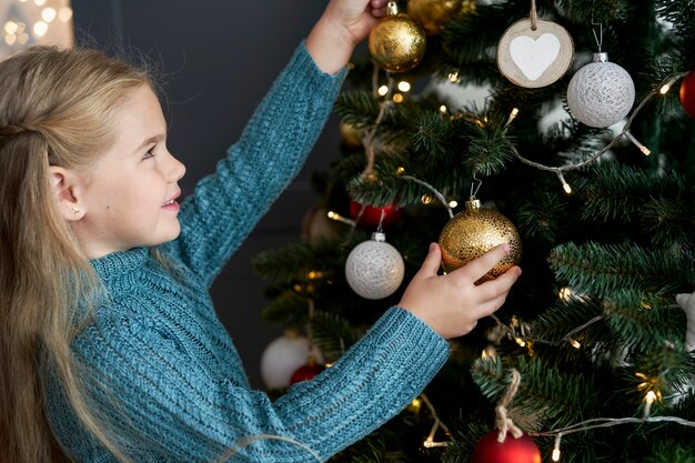 Linda chica adornos colgantes en el árbol de Navidad