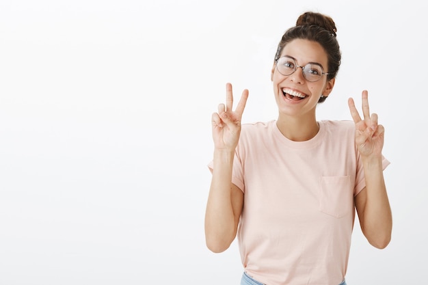 Linda chica alegre con gafas posando contra la pared blanca