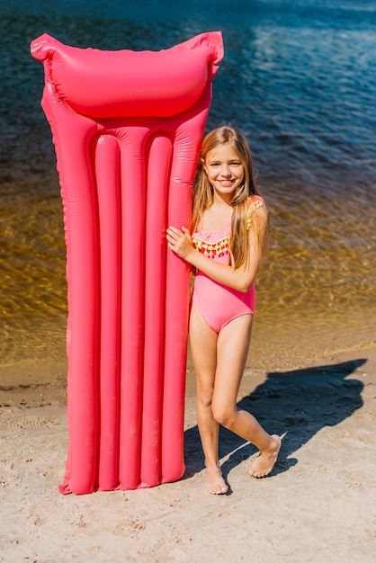 Linda chica con alfombra de aire de color en la orilla del mar