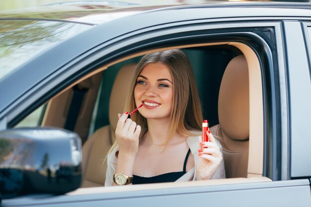 Linda chica aplicando lápiz labial en un coche