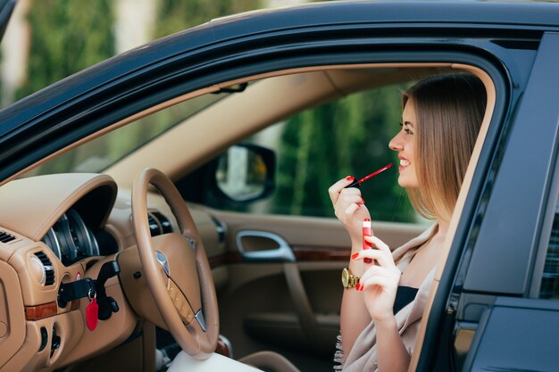 Linda chica aplicando lápiz labial en un coche