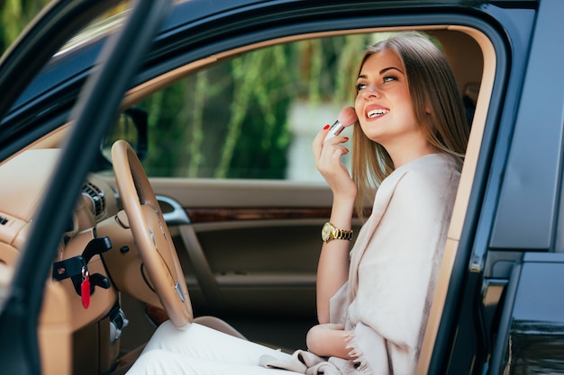 Linda chica aplicando lápiz labial en un coche