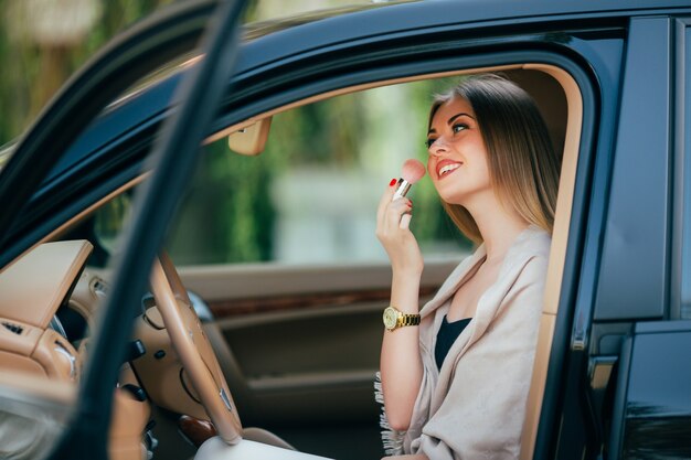 Linda chica aplicando lápiz labial en un coche