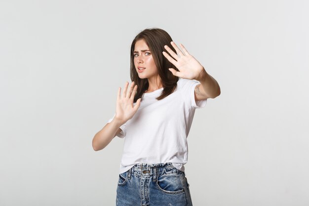 Linda chica asustada e insegura levantando las manos en gesto de parada, defendiéndose.