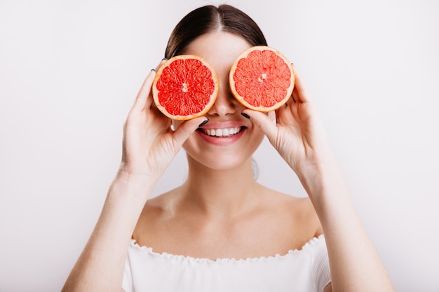 Linda chica atractiva de cabello oscuro con encantadora sonrisa posa, cubriendo sus ojos con pomelos.