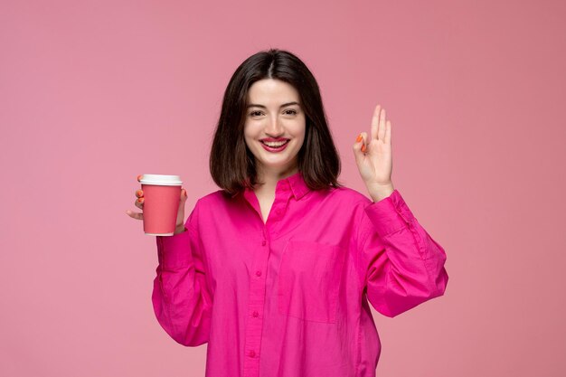 Linda chica bastante adorable en camisa rosa con lápiz labial rojo muy feliz por la taza de café rosa