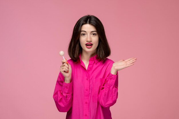 Linda chica bastante adorable chica en camisa rosa con lápiz labial rojo agitando las manos con piruleta redonda