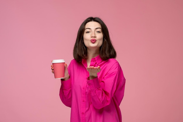 Linda chica bastante adorable chica en camisa rosa con lápiz labial rojo enviando besos con vaso de papel