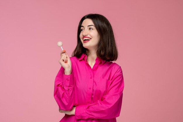 Linda chica bastante adorable chica en camisa rosa con lápiz labial rojo mirando hacia arriba con piruleta