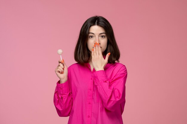 Linda chica bastante adorable chica en camisa rosa con lápiz labial rojo que cubre la boca con piruleta