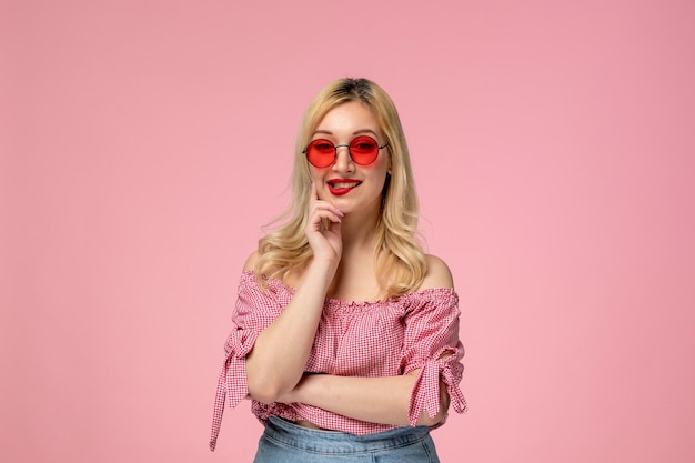 Linda chica bastante rubia con gafas rojas en camisa rosa mordiendo los labios con la cara feliz