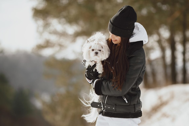 Linda chica caminando en un parque de invierno. Mujer con chaqueta marrón. Dama con un perro.
