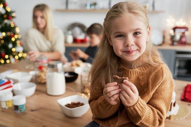 Linda chica comiendo galletas caseras mientras está sentado en la mesa