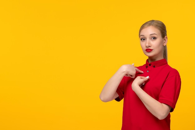 Linda chica del día de la camisa roja apuntándose a sí misma con una camisa roja sobre un fondo amarillo