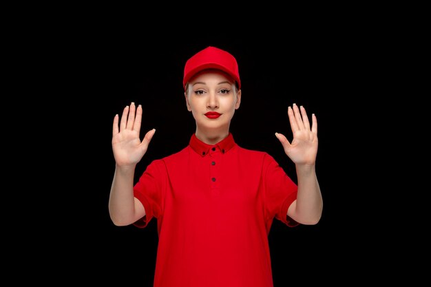 Linda chica del día de la camisa roja que muestra el símbolo de parada en una gorra roja con camisa y lápiz labial brillante