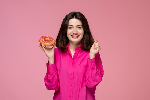 Linda chica encantadora adorable hermosa dama con lápiz labial rojo en camisa rosa muy emocionada por donut